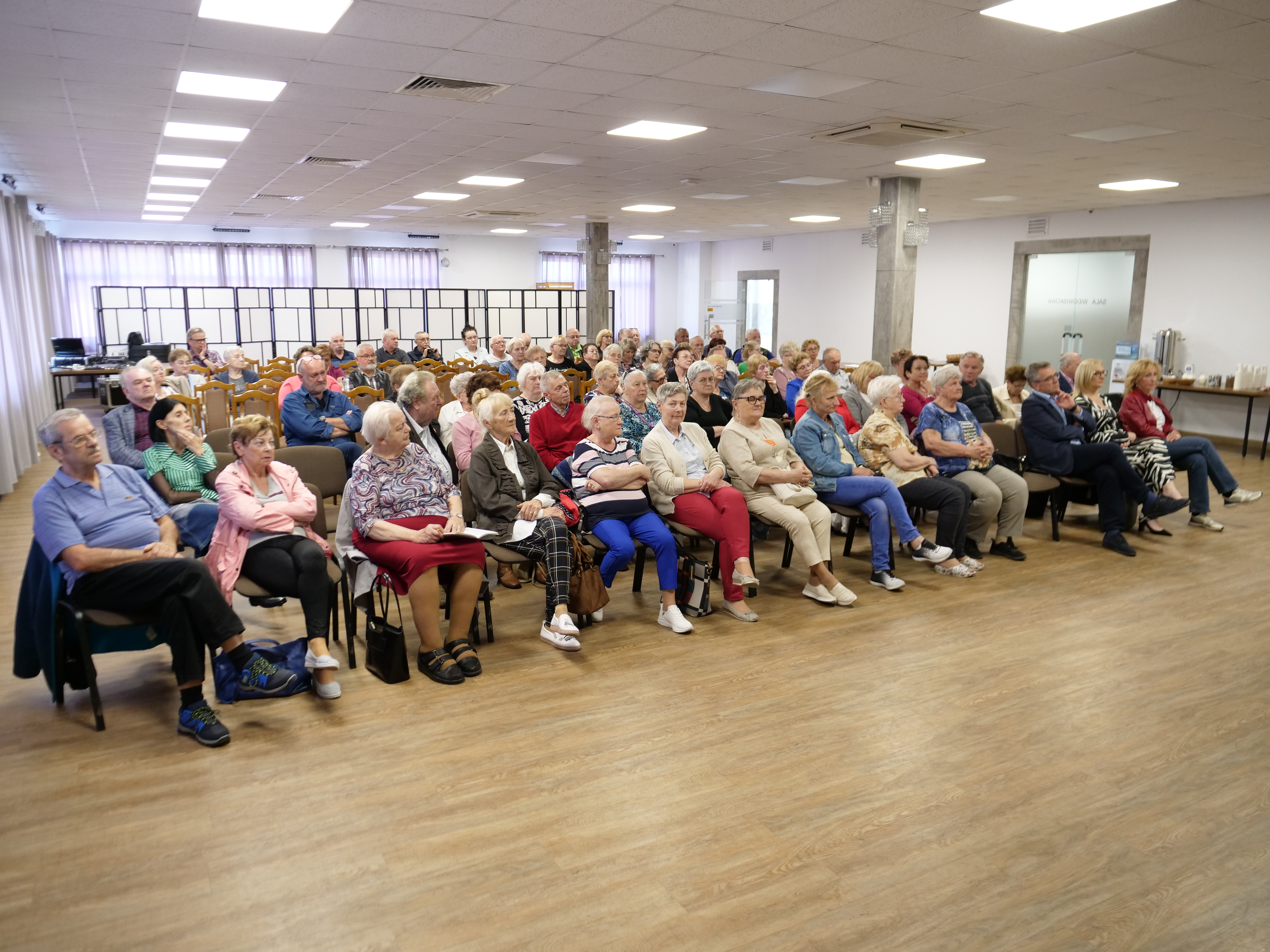 Grupa słuchaczy, siedzi na krzesłach. Ok. 70 os&oacute;b.